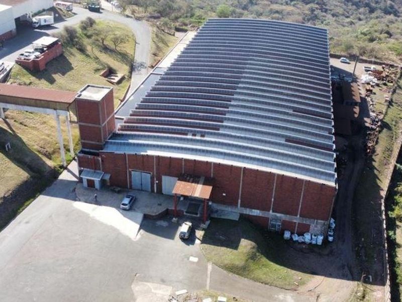 Aerial view of a large industrial warehouse facility featuring a corrugated metal roof, brick exterior, and an elevated connecting walkway.