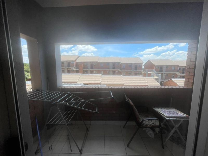 A covered balcony featuring tiled flooring and a brick balustrade, offering an outdoor space with views of the surrounding apartment complex.