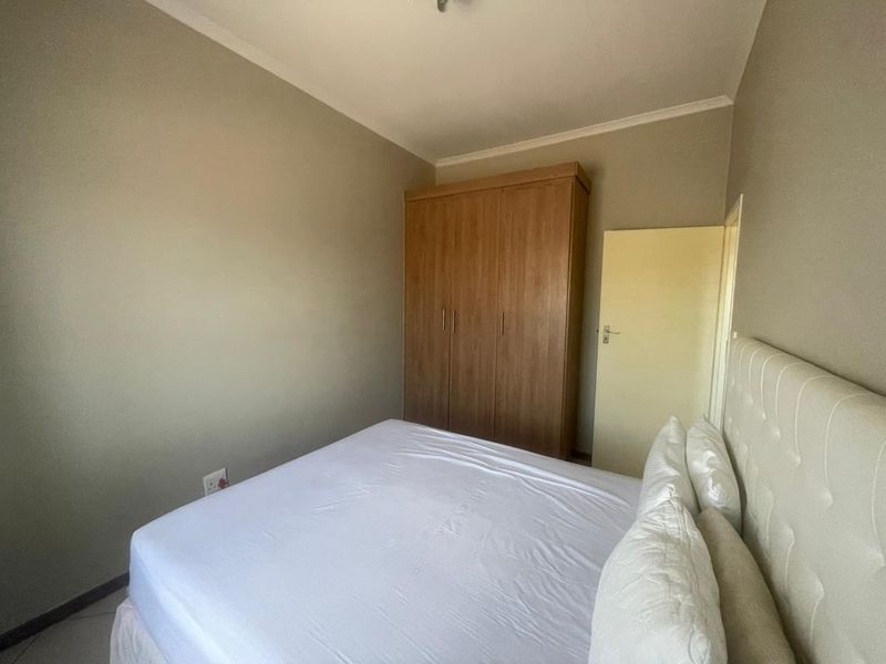 A functional bedroom featuring a built-in wooden wardrobe and neutral wall finishes, providing a clean and simple living space.