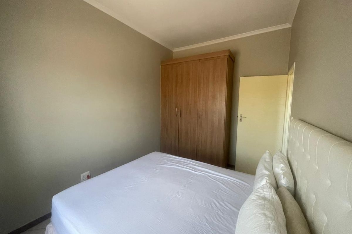 A functional bedroom featuring a built-in wooden wardrobe and neutral wall finishes, providing a clean and simple living space.