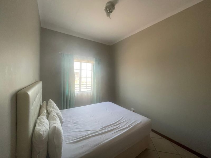 A simple bedroom featuring tiled flooring and a window with security bars, providing a functional and neutral space.
