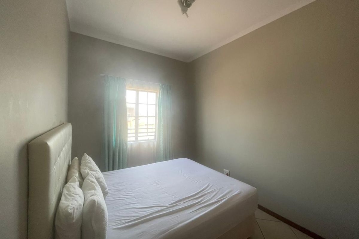 A simple bedroom featuring tiled flooring and a window with security bars, providing a functional and neutral space.