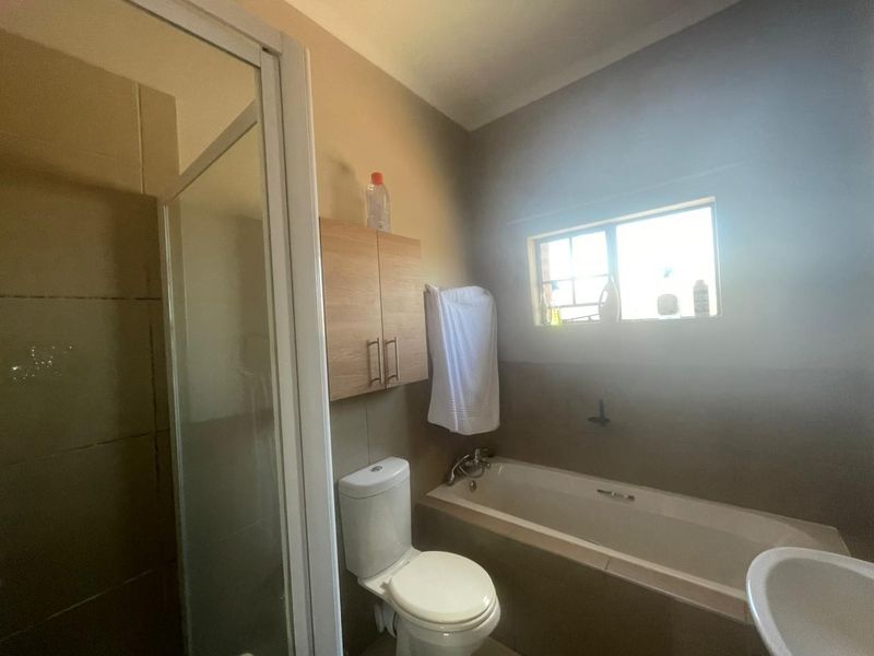 A functional bathroom featuring a shower enclosure, bathtub, toilet, and wall-mounted storage cabinet with neutral wall finishes.