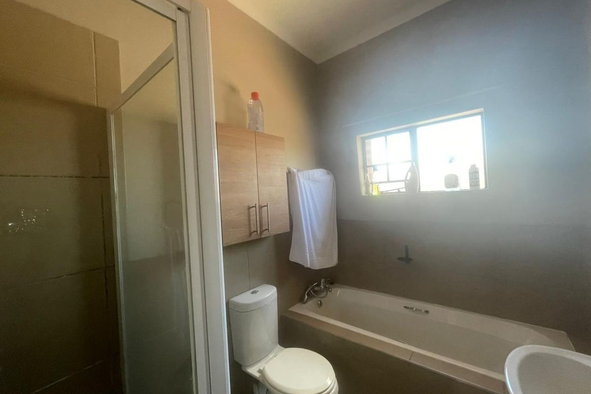 A functional bathroom featuring a shower enclosure, bathtub, toilet, and wall-mounted storage cabinet with neutral wall finishes.