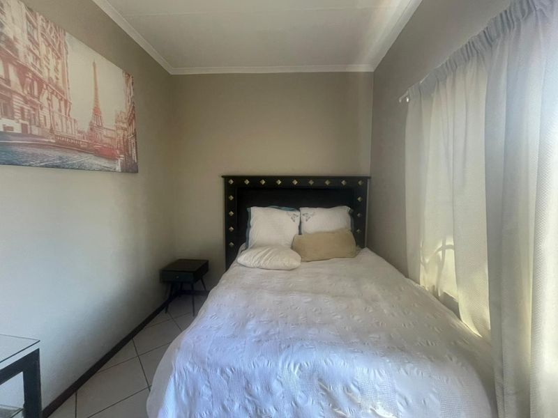 A compact bedroom featuring tiled flooring and neutral wall tones, providing a functional space with natural light from the window.