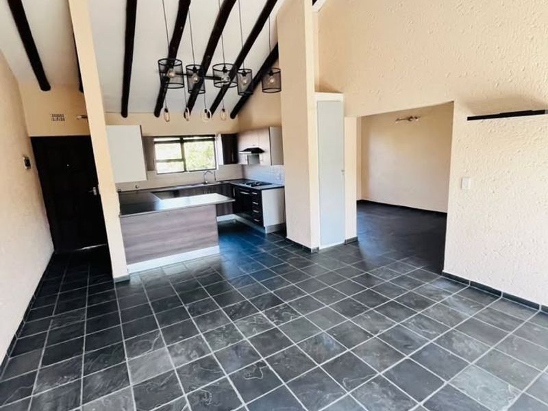 Spacious open-plan living and kitchen area featuring vaulted ceilings with exposed timber beams and durable slate tile flooring throughout.