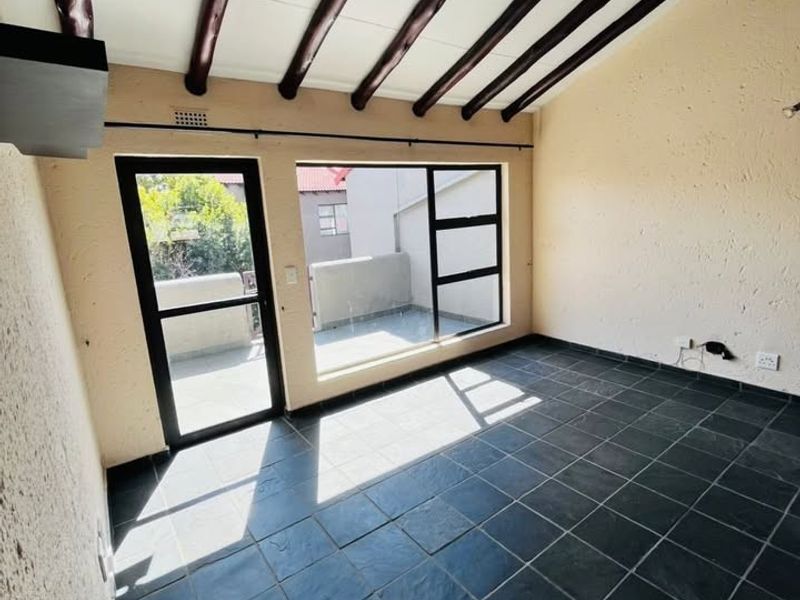 An empty living area featuring exposed timber ceiling beams, dark slate tile flooring, and direct access to an outdoor balcony through a glass door.