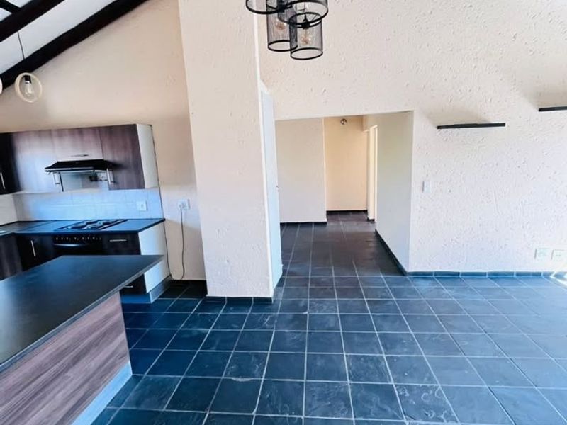 Spacious open-plan living and kitchen area featuring vaulted ceilings with exposed timber beams, slate tile flooring, and a modern kitchen island.
