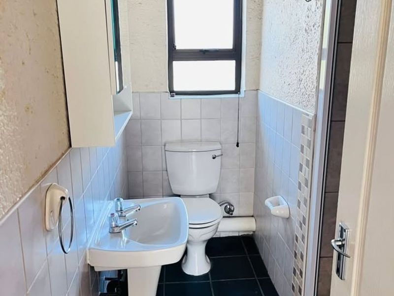 A compact bathroom featuring a pedestal basin, toilet, and shower enclosure with tiled walls and flooring.