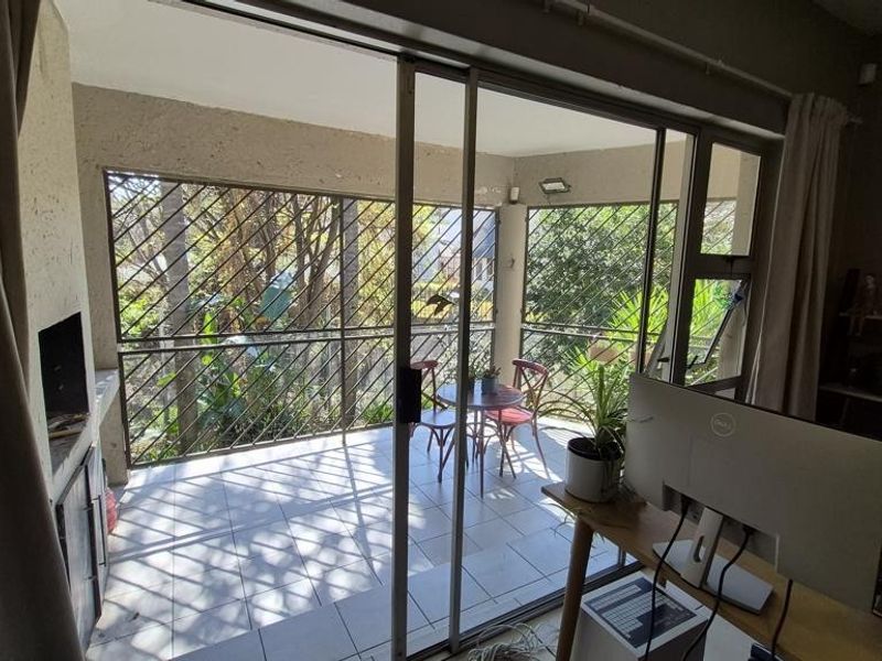 Covered balcony featuring a built-in braai, tiled flooring, and sliding glass doors providing access to the living area.