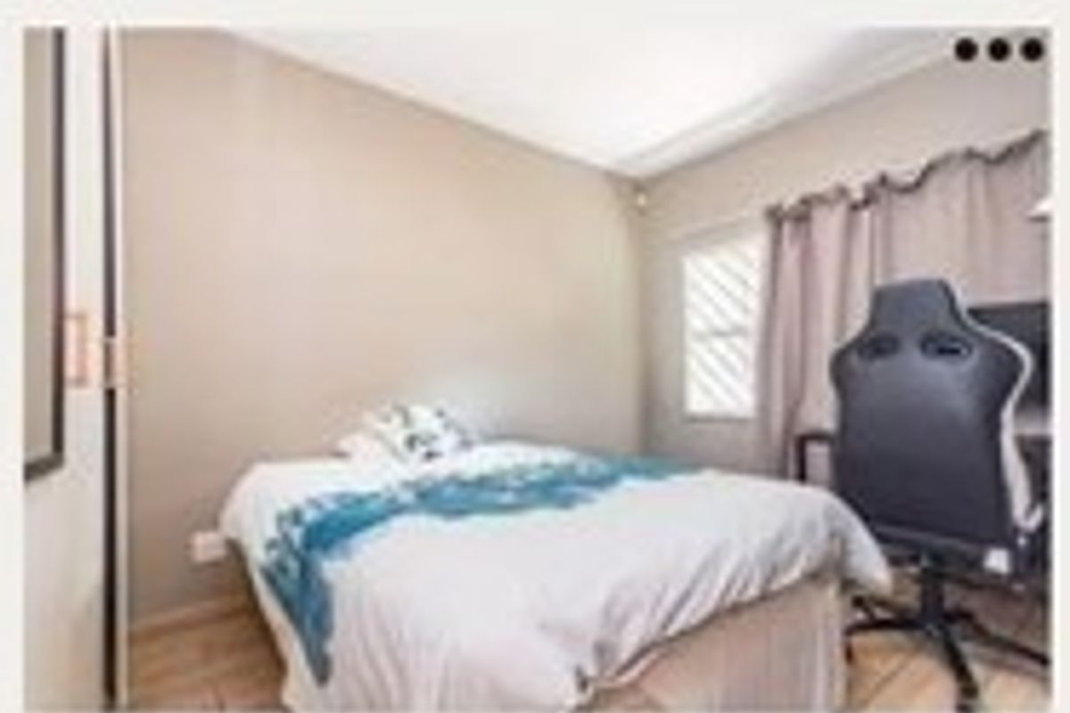 A compact bedroom featuring tiled flooring, a built-in cupboard, and a window fitted with security bars.