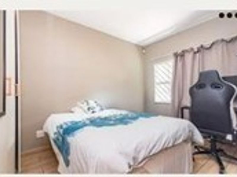 A compact bedroom featuring tiled flooring, a built-in cupboard, and a window fitted with security bars.