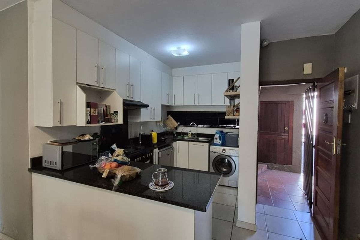 Compact kitchen featuring white cabinetry, granite countertops, and integrated laundry appliances, with direct access to an exterior entrance area.