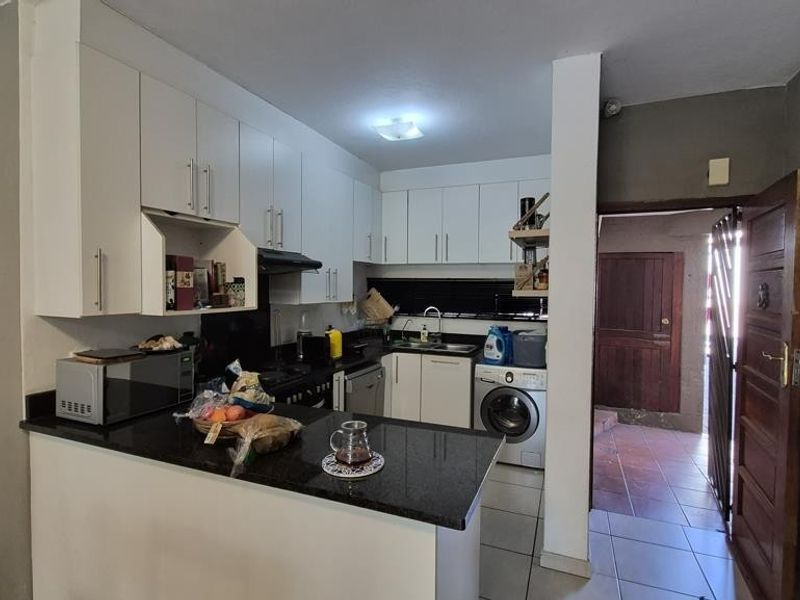 Compact kitchen featuring white cabinetry, granite countertops, and integrated laundry appliances, with direct access to an exterior entrance area.