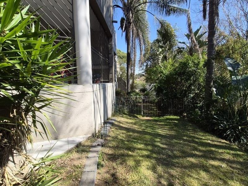 A private garden area featuring a lawn, mature trees, and a secure metal gate, adjacent to the apartment building's exterior wall.