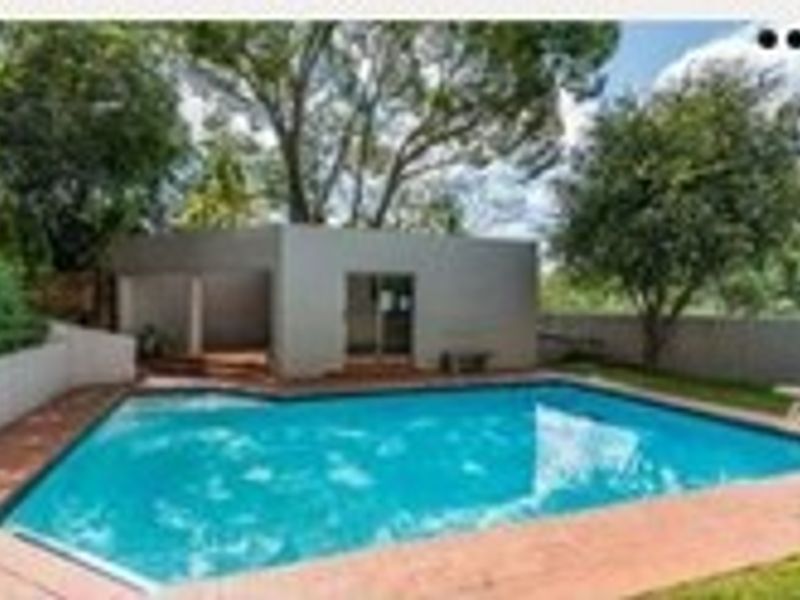 Outdoor pool area featuring a swimming pool, paved surround, and a covered patio structure set within a landscaped garden.