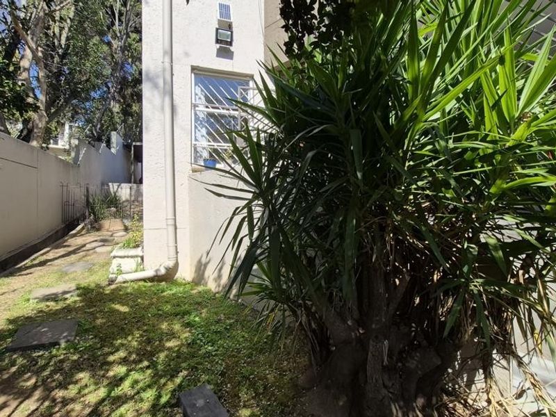 A view of the rear exterior area featuring a boundary wall, downpipe, and security bars on the window.