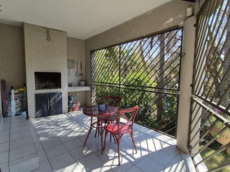 Covered balcony featuring a built-in braai, tiled flooring, and metal security screening, offering a functional outdoor entertainment space.