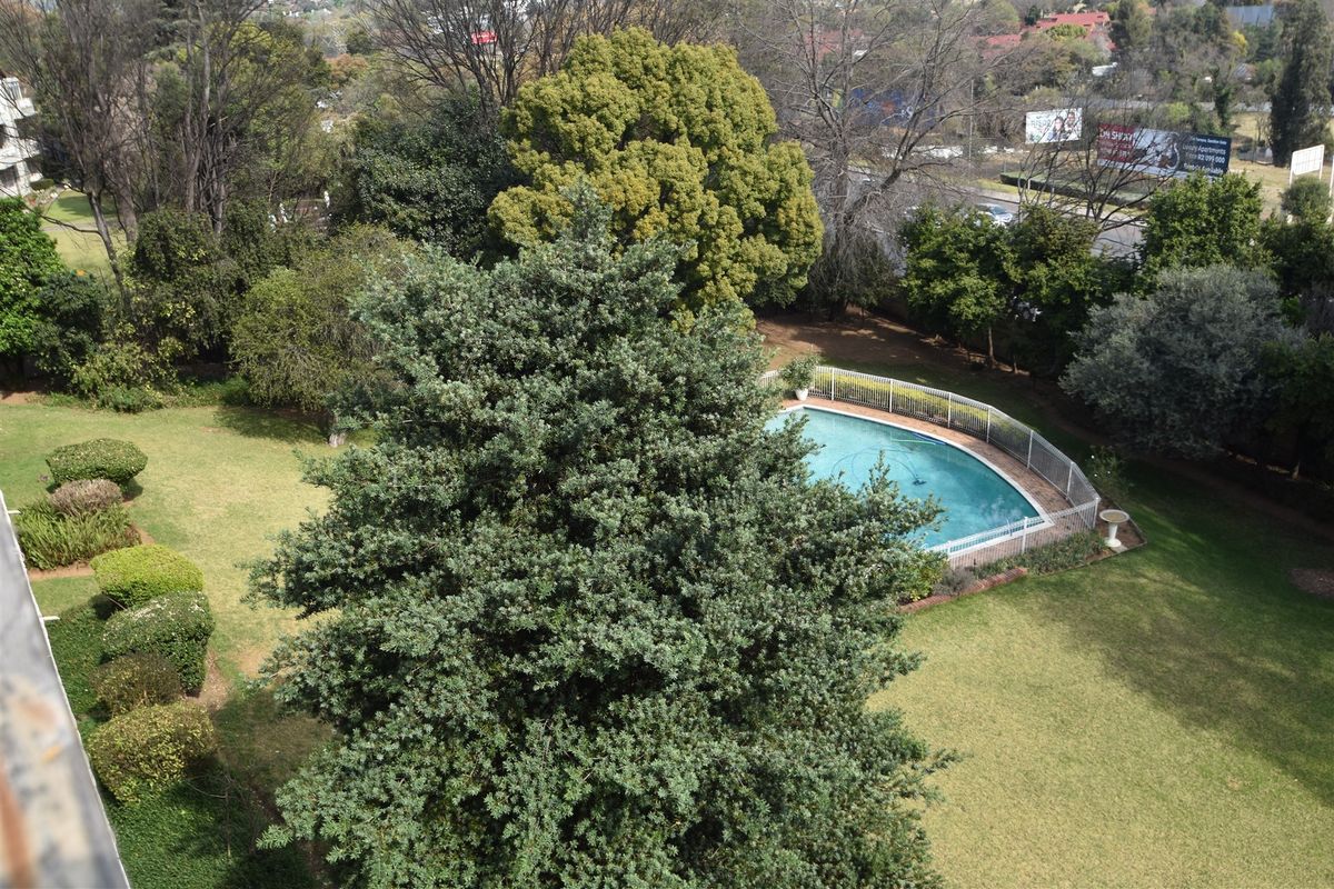 An elevated aerial view of a communal garden area featuring a swimming pool with safety fencing and mature trees.