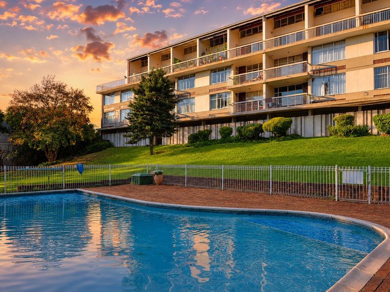 A view of the apartment complex exterior featuring a swimming pool, brick paved deck, and multi-level balconies at sunset.