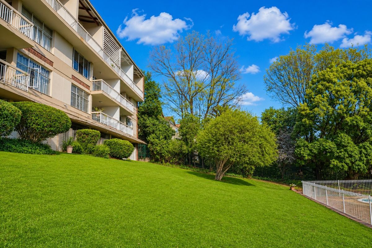 Rear view of the apartment building featuring multiple balconies, landscaped lawn, and pool area fencing.