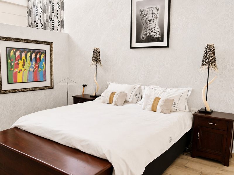 A well-maintained bedroom featuring neutral wallpaper, laminate flooring, and high ceilings, providing a comfortable and bright sleeping space.