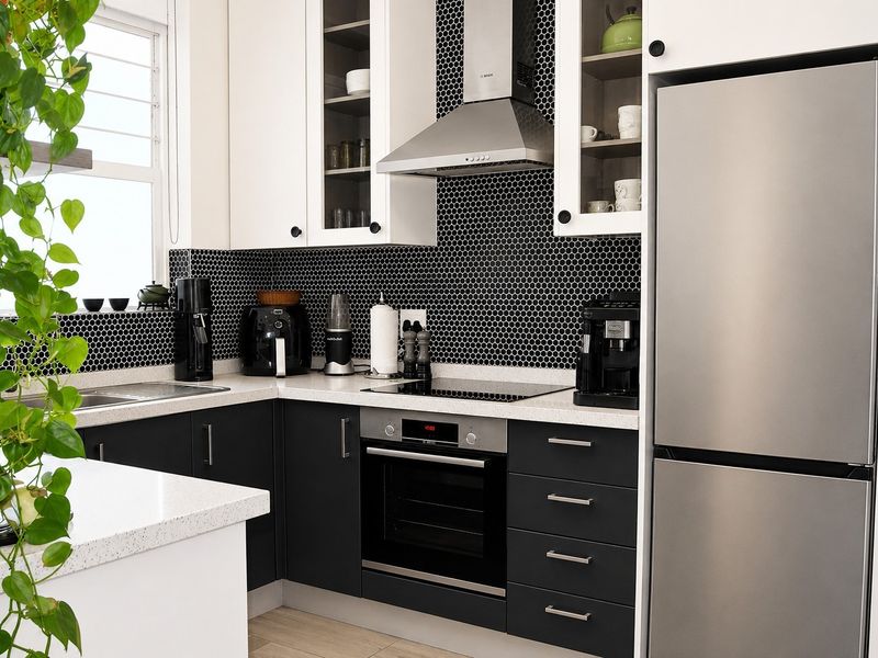 Modern kitchen featuring sleek black and white cabinetry, quartz countertops, a striking black mosaic tile backsplash, and integrated stainless steel appliances.