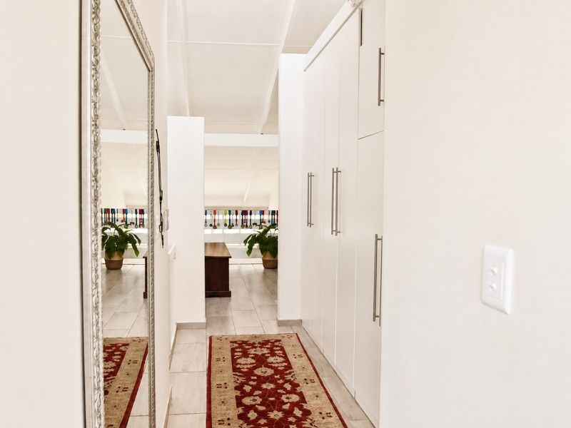 A bright, well-maintained hallway featuring extensive built-in storage cupboards and neutral tiled flooring, leading towards an open living area.