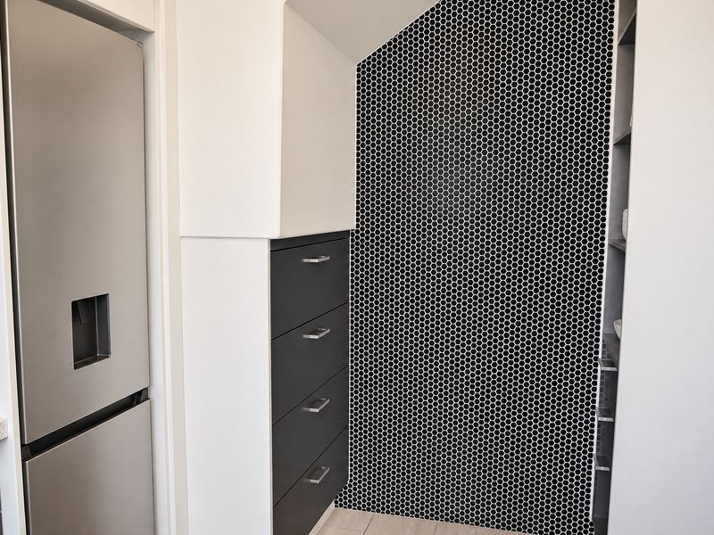 Modern kitchen area featuring sleek dark cabinetry, a striking black and white mosaic tile feature wall, and integrated refrigerator.