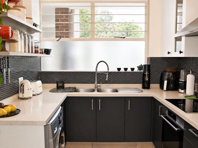 Modern U-shaped kitchen featuring dark cabinetry, stone benchtops, a striking black mosaic splashback, and integrated stainless steel appliances.