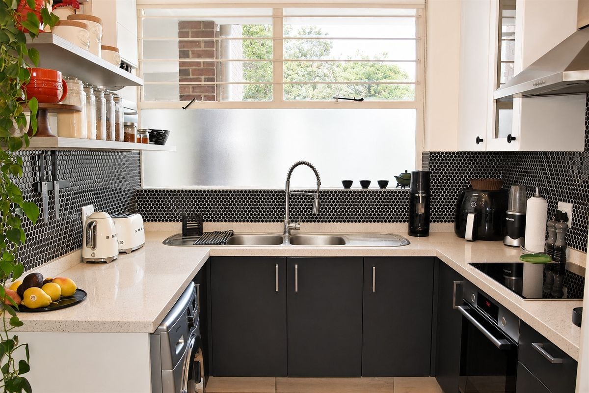 Modern U-shaped kitchen featuring dark cabinetry, stone benchtops, a striking black mosaic splashback, and integrated stainless steel appliances.