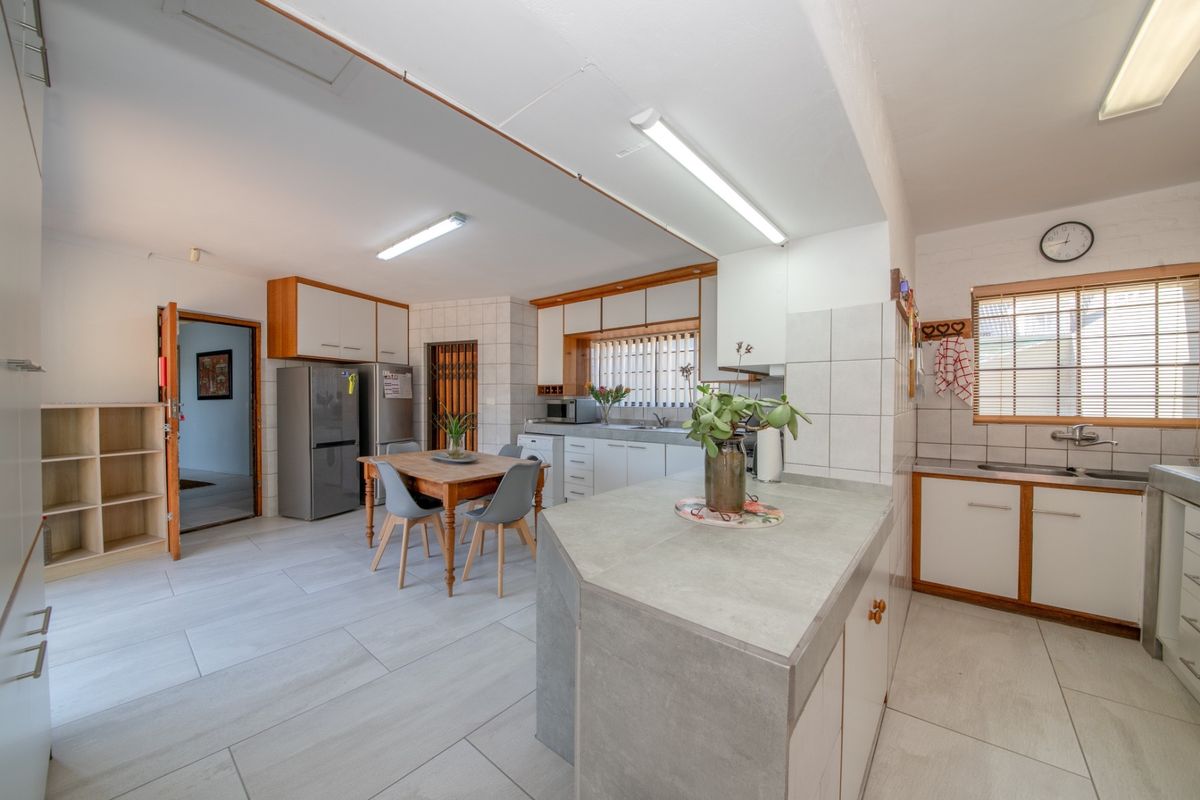 A functional kitchen featuring tiled flooring, ample built-in cabinetry, a stone-look countertop, and a double sink with a tiled backsplash.