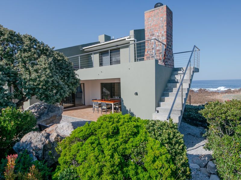 Rear view of a coastal home featuring a covered patio, external staircase with stainless steel railing, and a prominent brick chimney.