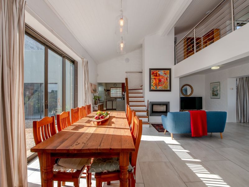 Spacious open-plan living and dining area featuring high ceilings, a fireplace, tiled floors, and a mezzanine level with a modern stainless steel balustrade.