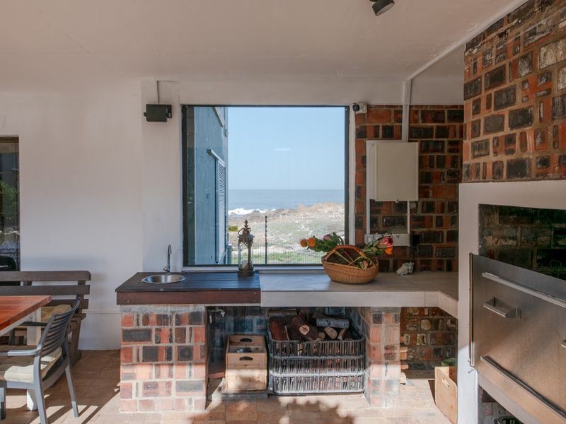 Covered patio area featuring a built-in brick braai, concrete prep counter with integrated sink, and direct ocean views.