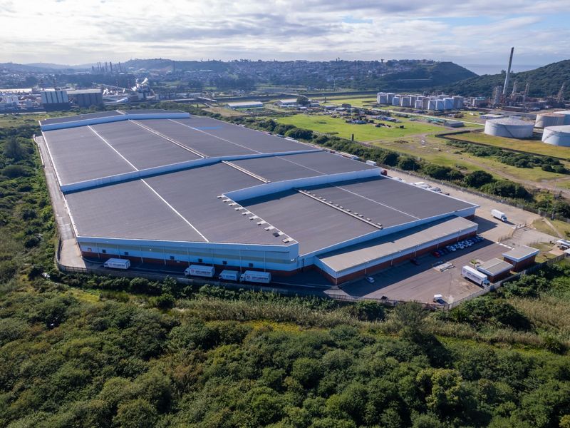 Aerial view of a large industrial warehouse facility featuring extensive roof space, a paved loading yard, and secure perimeter fencing.