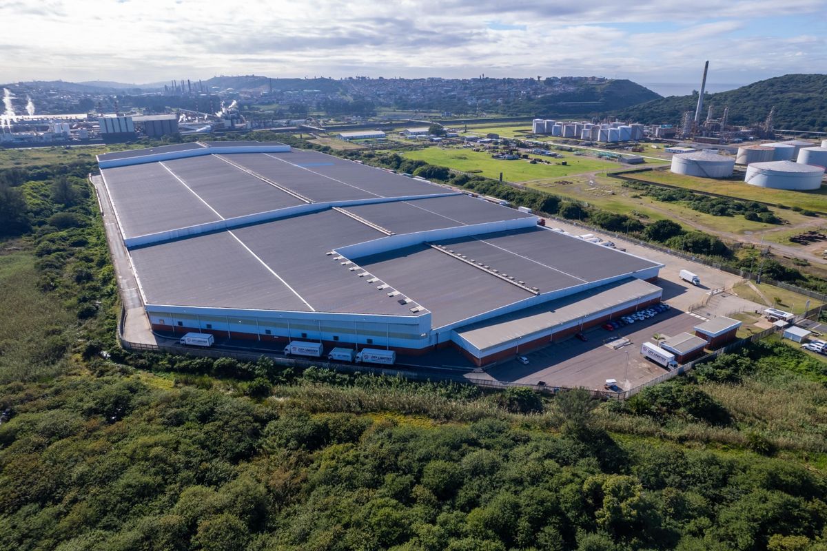 Aerial view of a large industrial warehouse facility featuring extensive roof space, a paved loading yard, and secure perimeter fencing.