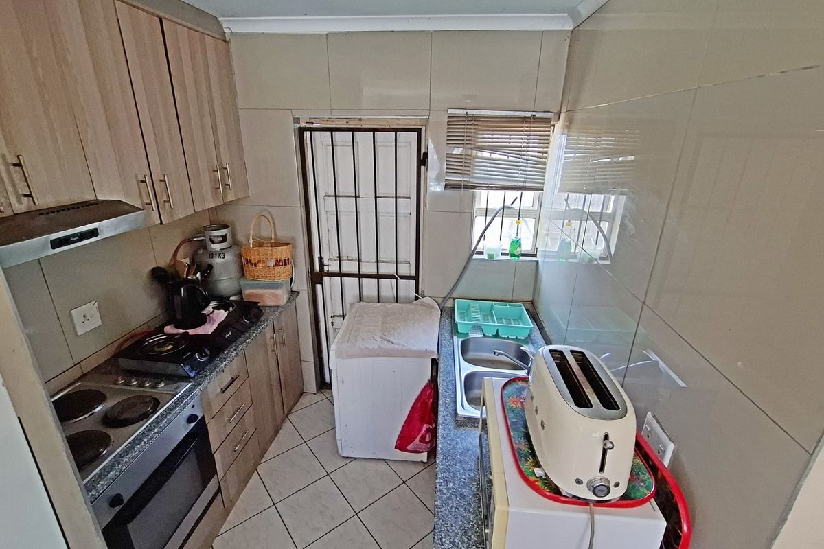 Compact kitchen featuring built-in cabinetry, tiled walls, a double sink, and integrated cooking appliances with direct access to an exterior security door.