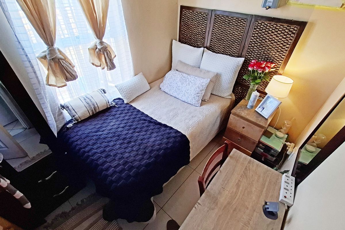 A compact bedroom featuring tiled flooring and a decorative built-in headboard, offering a functional space with natural light from the adjacent window.