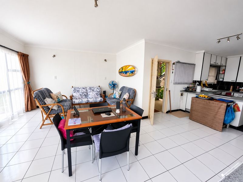 Open-plan living and dining area featuring white tiled flooring, integrated kitchen cabinetry, and a sliding glass door providing natural light.