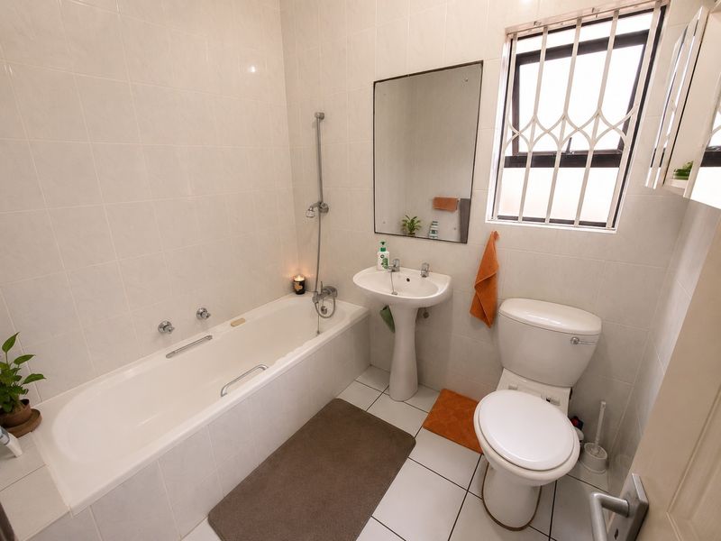 A functional bathroom featuring a pedestal basin, bathtub with shower mixer, and toilet, finished with neutral wall and floor tiles.