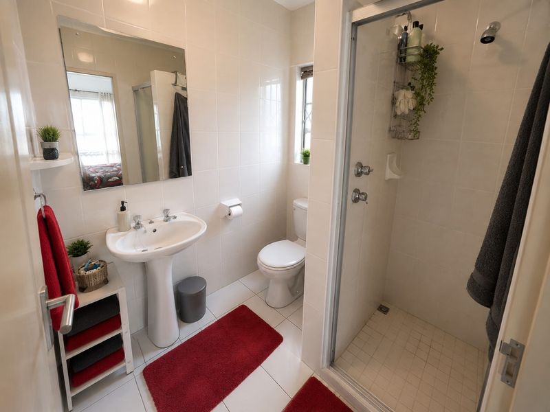 A functional bathroom featuring a pedestal basin, a glass-enclosed shower, and a toilet, finished with neutral wall and floor tiles.
