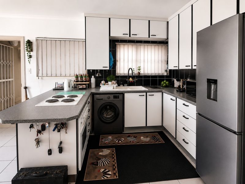 A functional kitchen featuring white cabinetry with black trim, dark laminate countertops, a built-in electric hob, and a tiled backsplash.