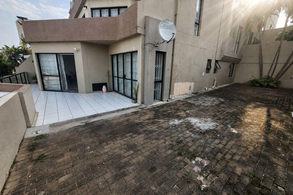 Rear exterior view of the apartment featuring a tiled patio area and a paved courtyard with visible wear on the exterior finishes.
