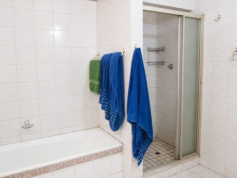 A functional bathroom featuring a built-in bathtub, a separate shower enclosure with a sliding door, and fully tiled walls and flooring.