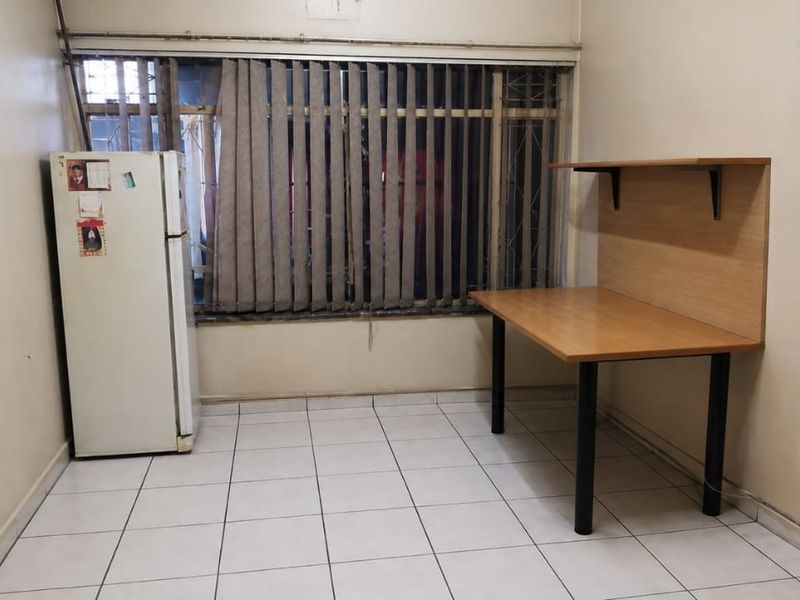 A bedroom featuring tiled flooring, built-in cupboards, and security bars on the window. The room requires cosmetic updates to the walls and finishes.
