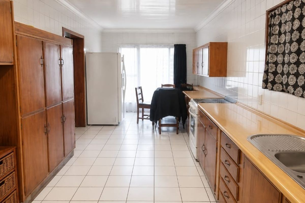 A functional kitchen featuring wooden cabinetry, tiled splashbacks, and a double bowl stainless steel sink, offering a classic layout with potential for modernization.