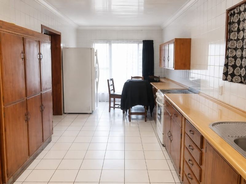 A functional kitchen featuring wooden cabinetry, tiled splashbacks, and a double bowl stainless steel sink, offering a classic layout with potential for modernization.