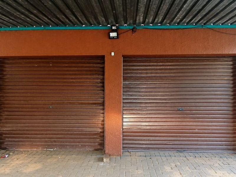 A double garage featuring brown roller doors, a corrugated metal roof, and paved driveway access, providing secure off-street parking.