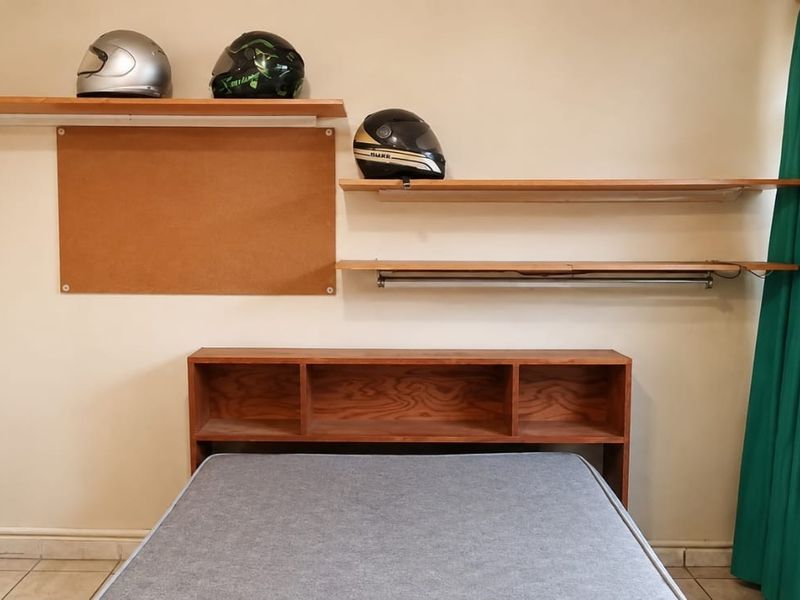 A bedroom featuring built-in wooden shelving and a matching headboard, complemented by tiled flooring and window curtains.